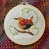 Embroidery hoop with a cross-stitched wren on a textured fabric background