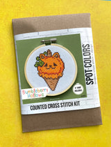 Cross stitch kit packaging with a pumpkin design on a yellow background