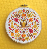 Cross-stitched pattern with an owl and autumn leaves in a hoop on a yellow background