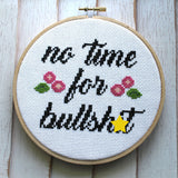 Cross-stitched hoop with 'no time for bullsh*t' text and decorative elements on a wooden background