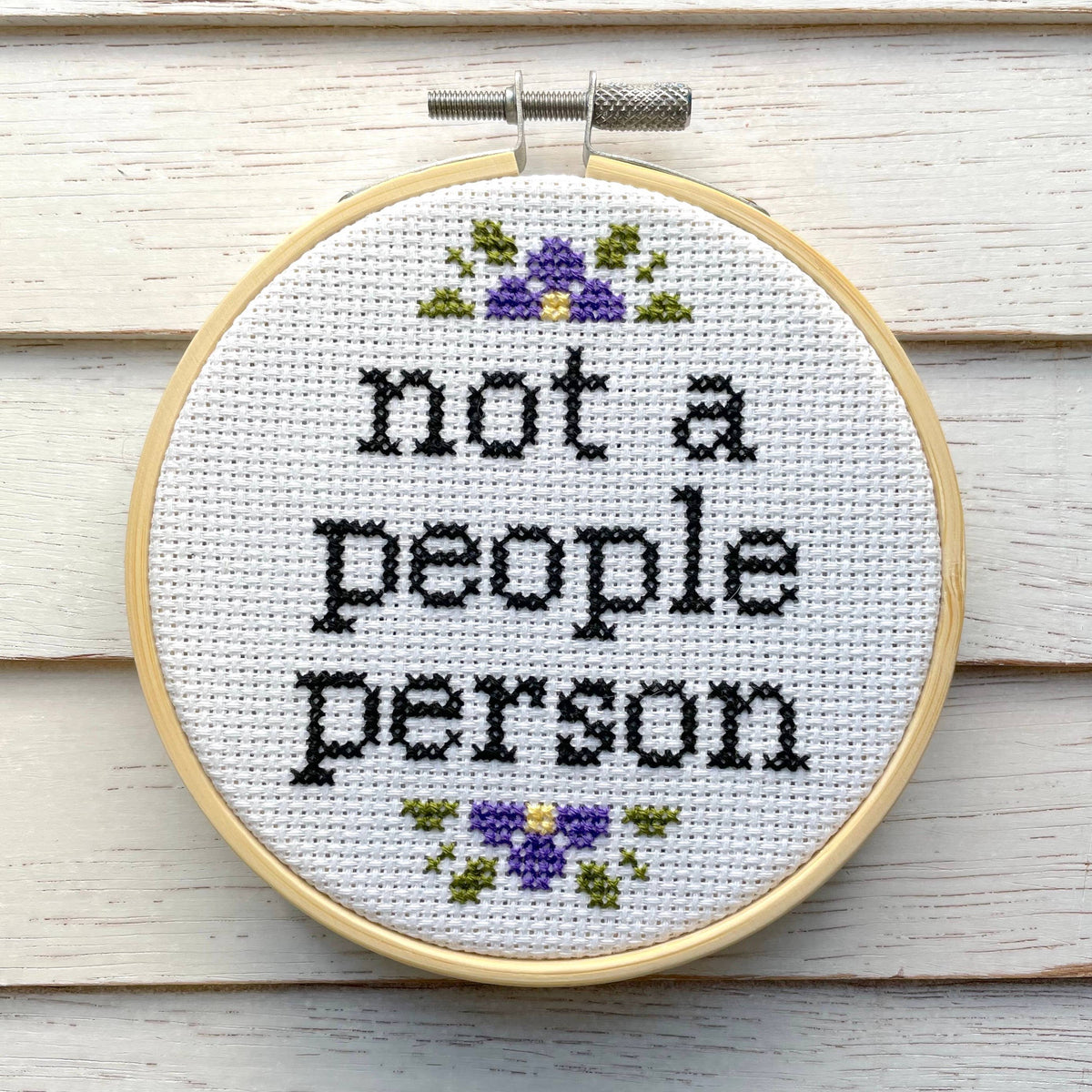 Cross-stitched hoop with 'not a people person' text on a wooden background