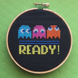 Embroidery hoop with cross-stitched design of Pac-Man ghosts and 'READY!' text on a green background
