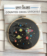 Counted cross stitch kit with space-themed design on a wooden surface