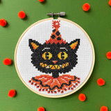 Embroidery hoop with a black cat design on a green background with red pom-poms.