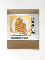 Cross stitch kit packaging with a bear on pancakes design on a white background