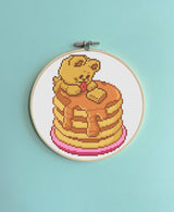 Embroidery hoop with a teddy bear on pancakes design against a light blue background