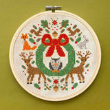 Cross-stitched wreath with animals in an embroidery hoop on a green background