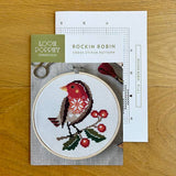 Cross stitch kit with a completed design of a robin bird on a wooden surface