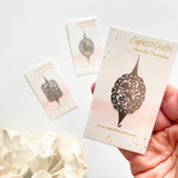 Hand holding a card with 'Eight22Crafts' branding and needle threader illustration on a light background.