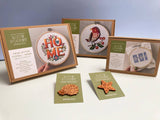 Embroidery kits with 'HOME' design and other decorative items on a white surface.
