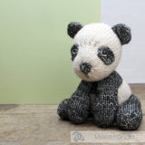 Knitted panda toy on a wooden surface with a green and white background