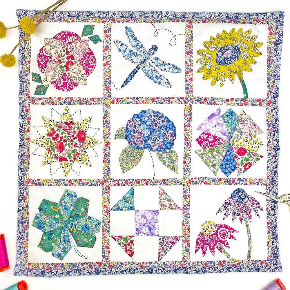 Colorful quilt with floral and nature-themed blocks on a white background