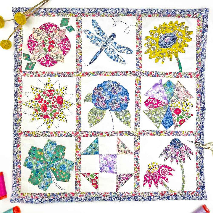 Colorful quilt with floral and nature-themed blocks on a white background
