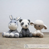 Three knitted animal toys (rabbit, panda, sheep) on a wooden surface with a light gray background.