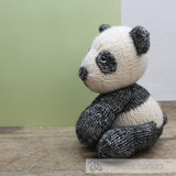 Knitted panda toy on a wooden surface with a green and white background