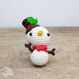 Crocheted snowman toy with a top hat, scarf, and carrot nose on a wooden surface.