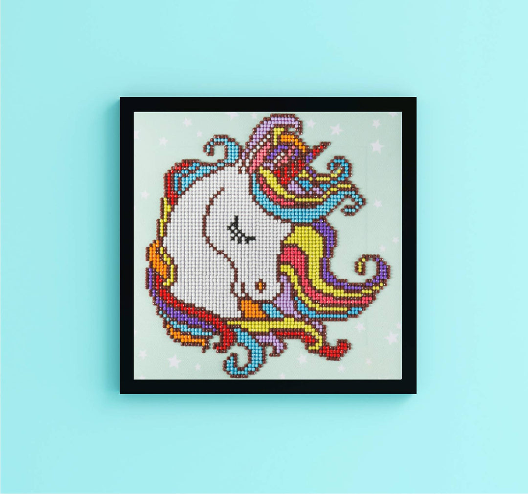 Framed colorful unicorn cross-stitch on a light blue background