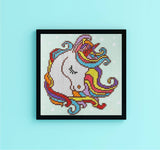 Framed colorful unicorn cross-stitch on a light blue background