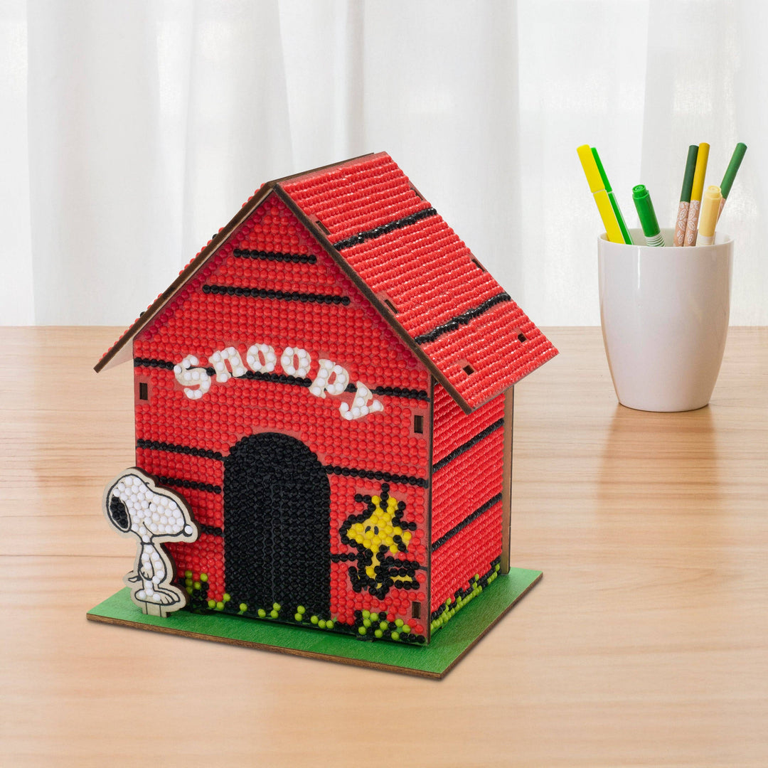 Red doghouse with 'Snoopy' branding on a wooden surface with a white curtain background.