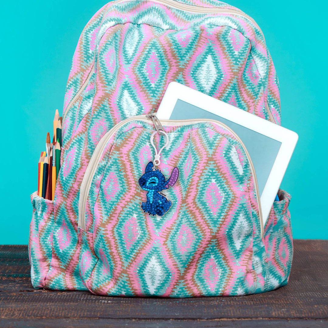 Backpack with pink and blue geometric pattern, containing stationery items and a tablet, on a teal background.