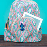 Backpack with pink and blue geometric pattern, containing stationery items and a tablet, on a teal background.