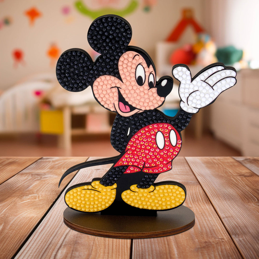 Mickey Mouse figurine made of interlocking bricks on a wooden surface with a blurred colorful background.