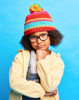 Child wearing a colorful striped beanie and yellow sweater against a blue background