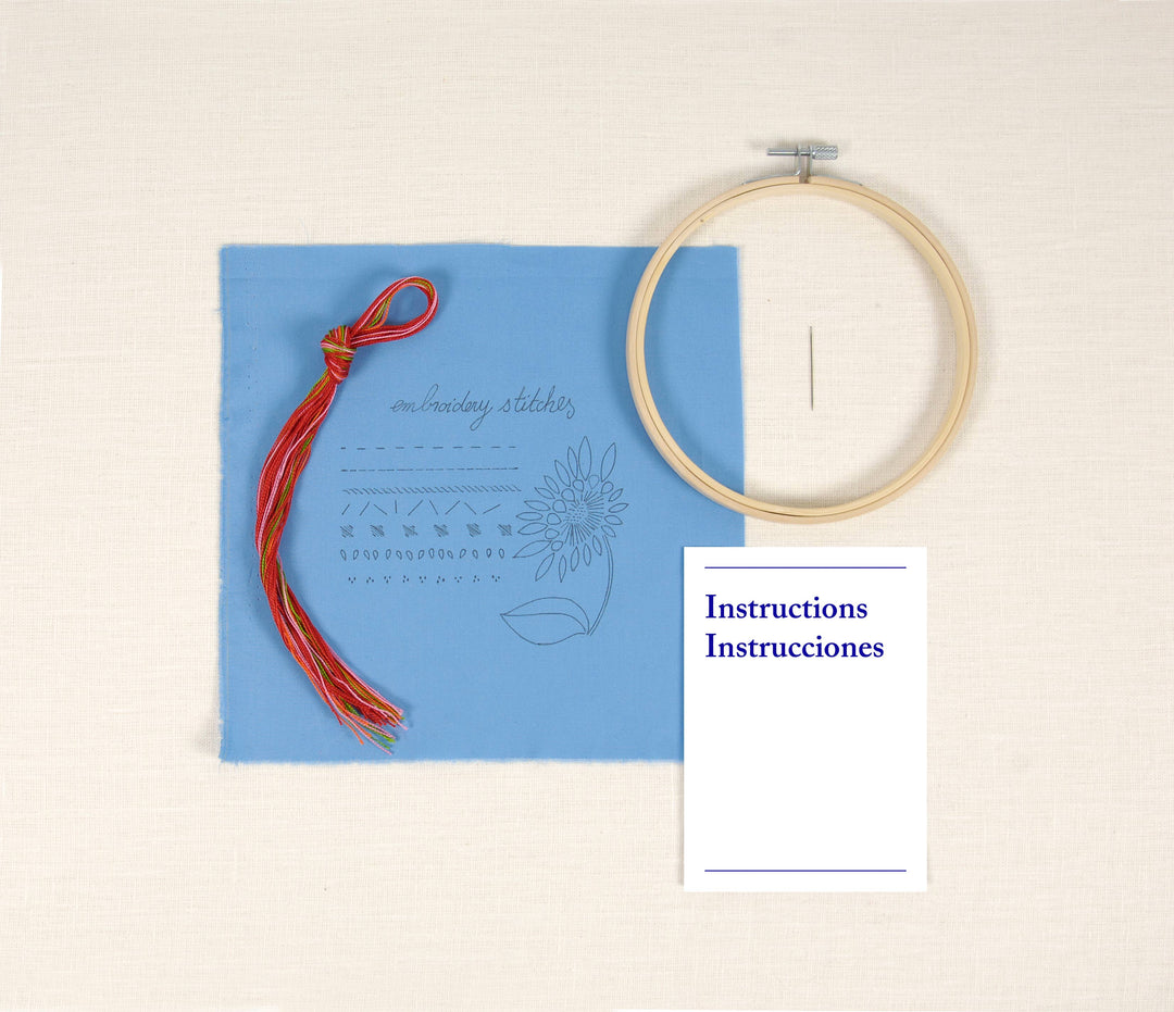 Embroidery hoop, blue card with floral design, and red thread on a beige background