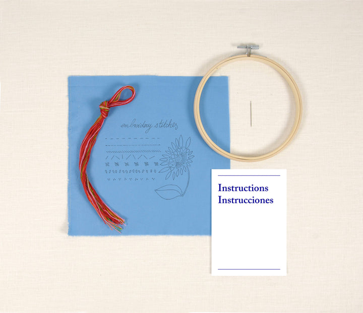 Embroidery hoop, blue card with floral design, and red thread on a beige background