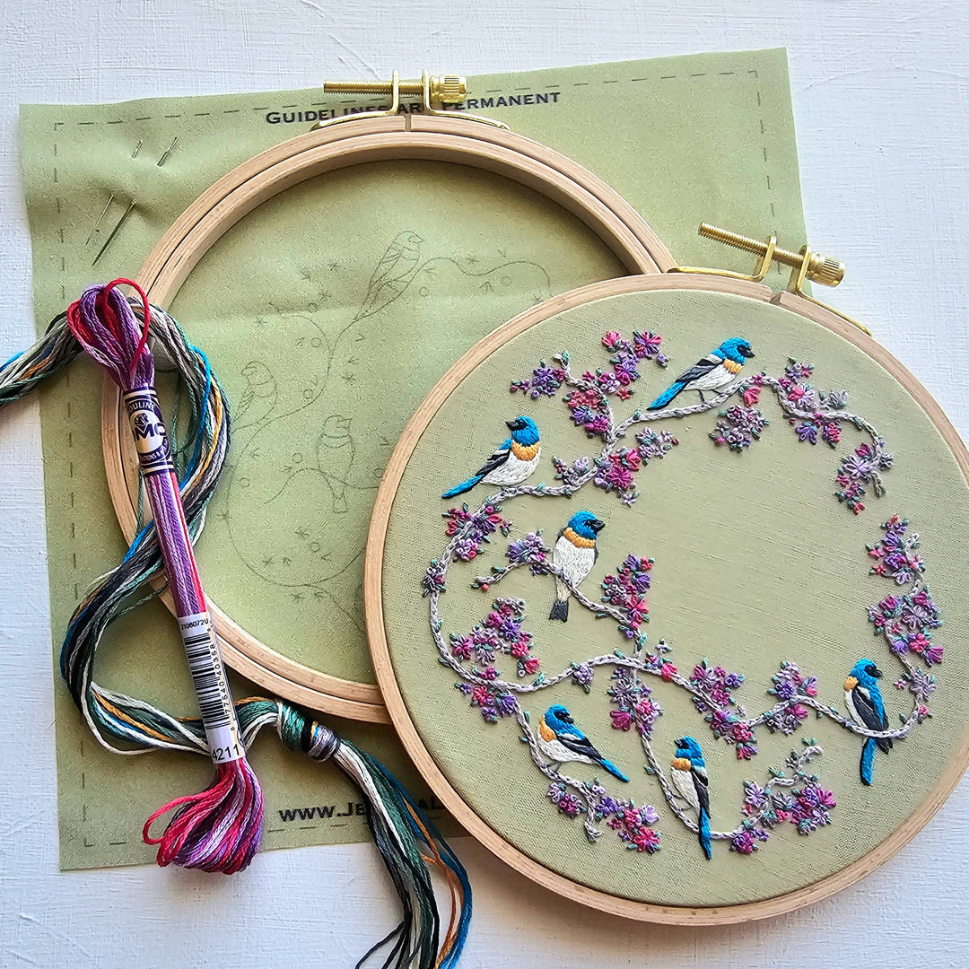 Embroidery hoop with bird and floral design on green fabric, with embroidery thread and pattern guide.