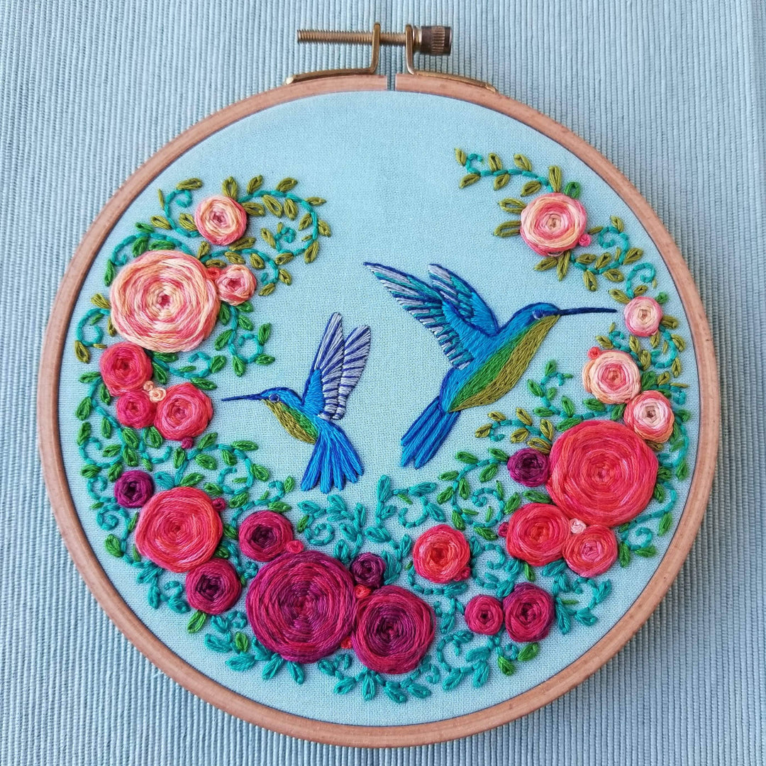 Embroidery hoop with floral design and hummingbirds on a light blue background