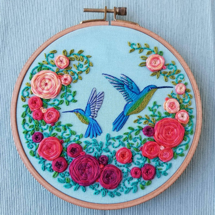 Embroidery hoop with floral design and hummingbirds on a light blue background