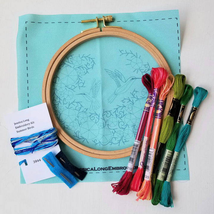 Embroidery hoop with colorful threads and a pattern on a light blue mat.