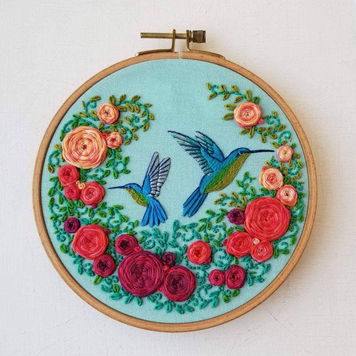 Embroidery hoop with colorful floral and hummingbird design on a light blue background