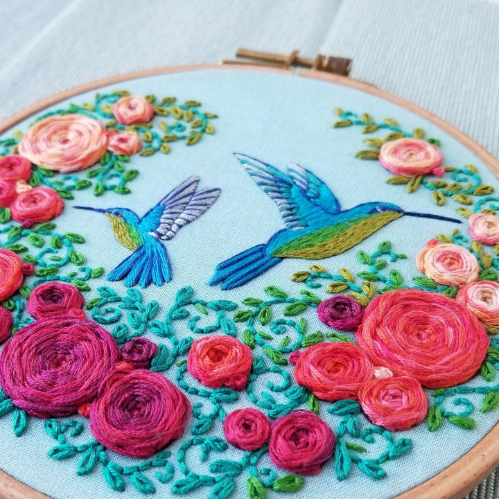 Embroidery hoop with colorful floral and hummingbird design on a light blue background