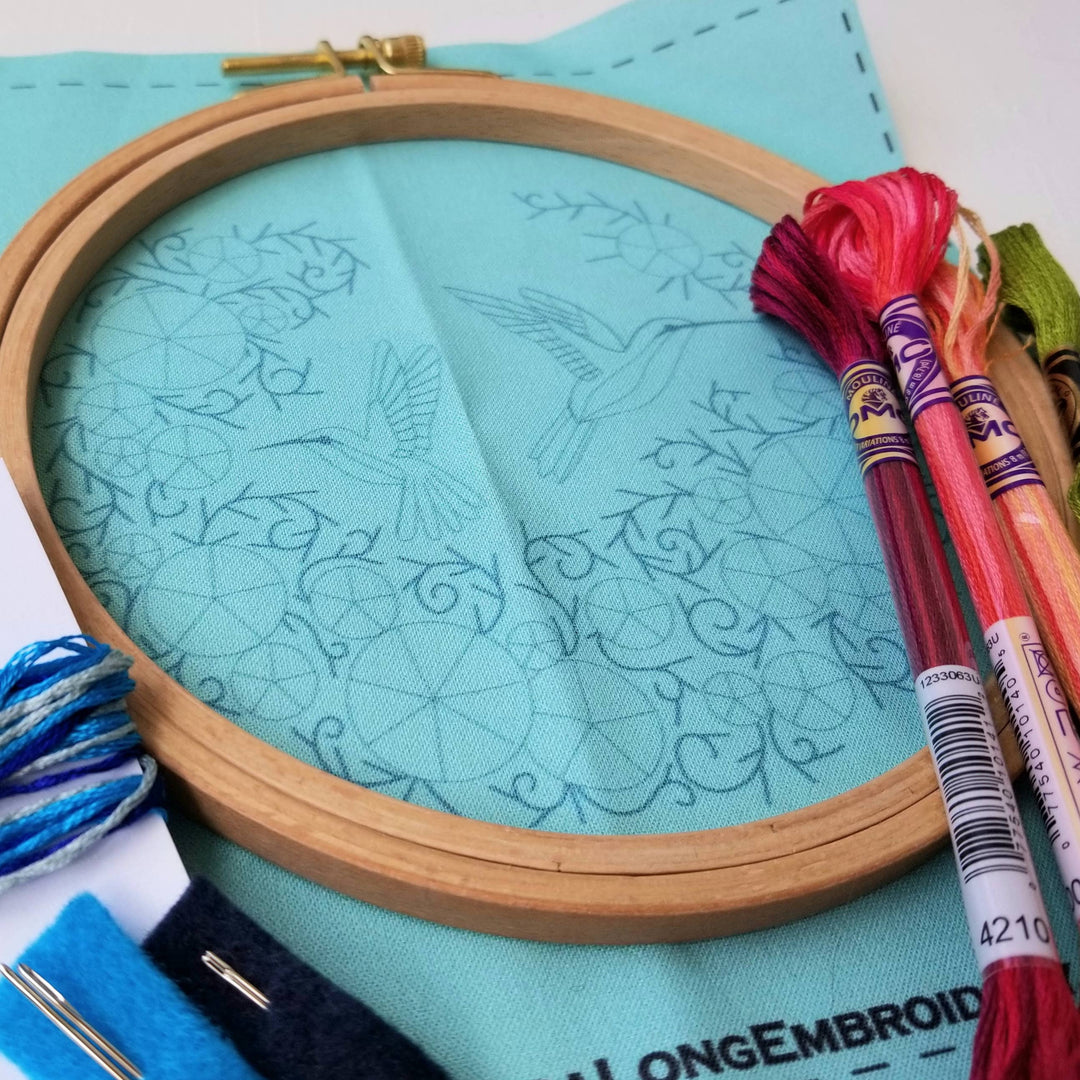 Embroidery hoop with patterned fabric and colorful threads on a light blue background