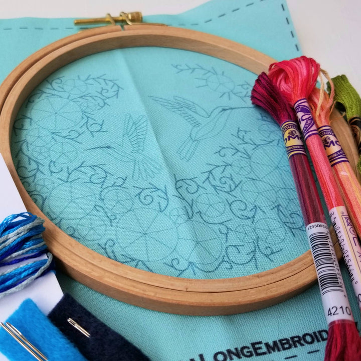Embroidery hoop with patterned fabric and colorful threads on a light blue background