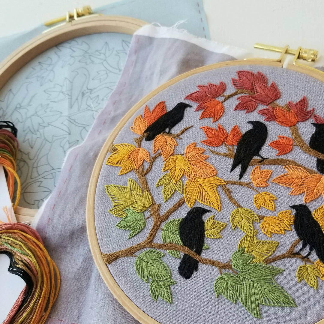 Embroidery hoop with autumn-themed design featuring leaves and birds.