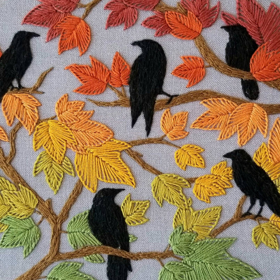 Embroidery of black birds on branches with colorful leaves