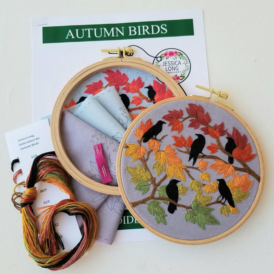 Embroidery hoops with autumn-themed designs and supplies on a white background