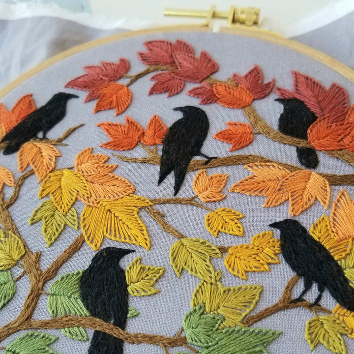 Embroidery hoop with autumn-themed design featuring leaves and birds.
