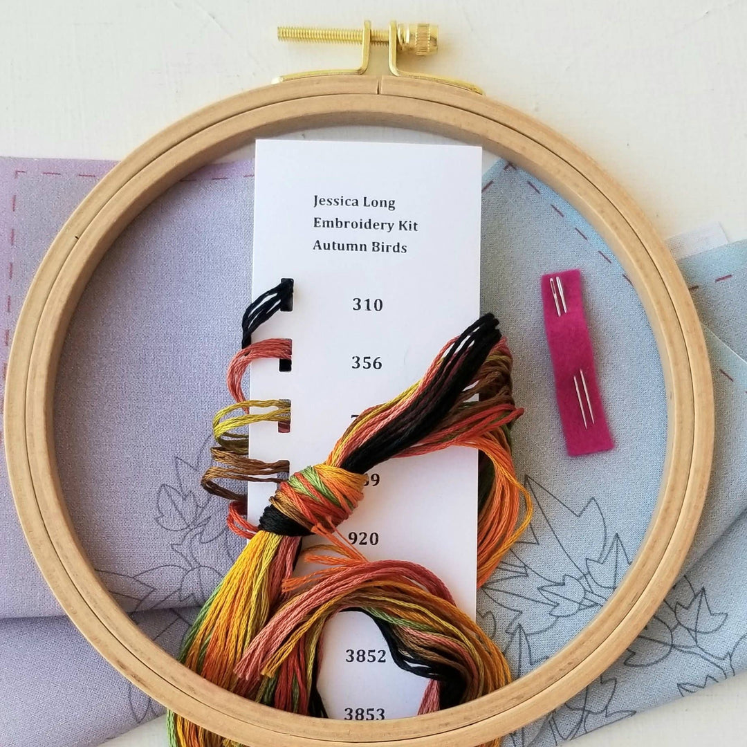 Embroidery hoop with colorful threads and a kit label on a light background