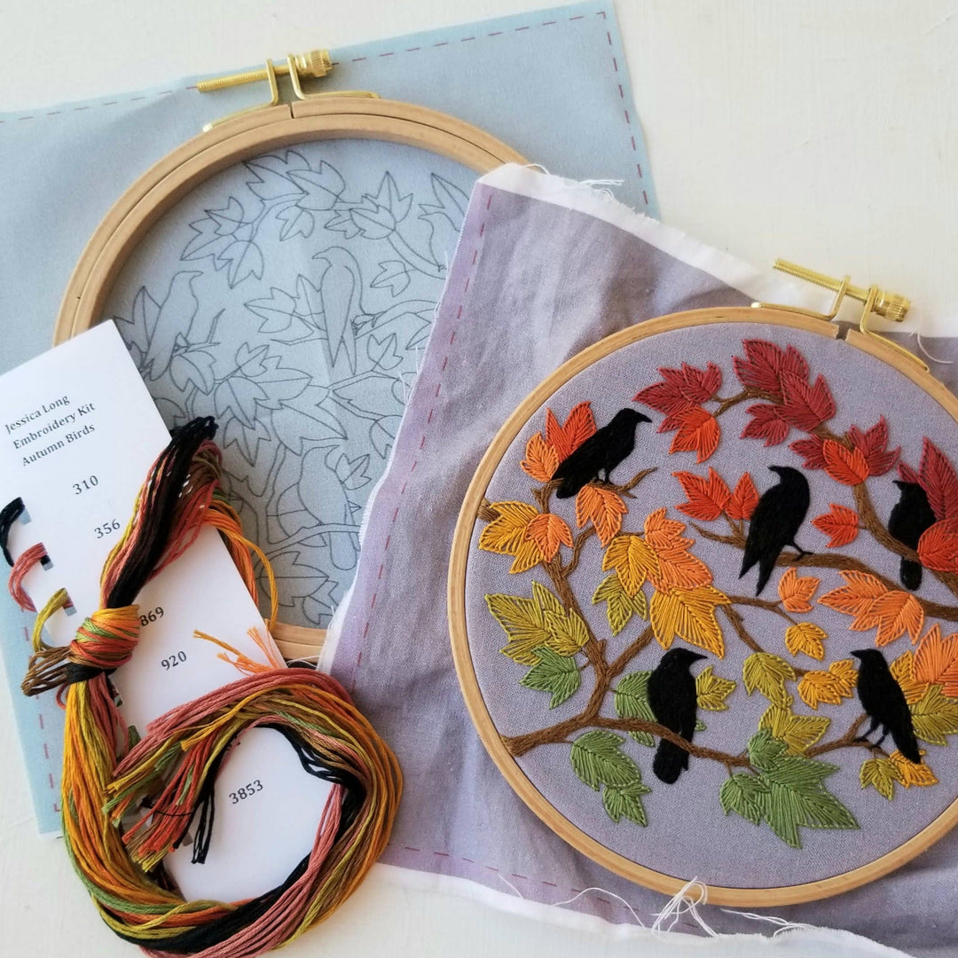 Embroidery hoop with autumn-themed embroidery and colorful threads on a light blue fabric background.