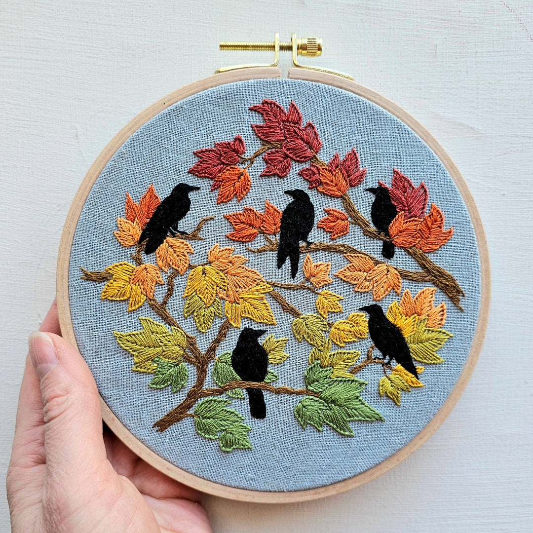 Embroidery hoop with autumn-themed design featuring birds and leaves.