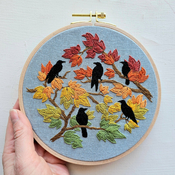 Embroidery hoop with autumn-themed design featuring birds and leaves.