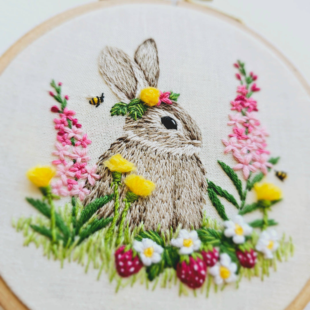 Embroidery of a rabbit surrounded by flowers and plants in an embroidery hoop.