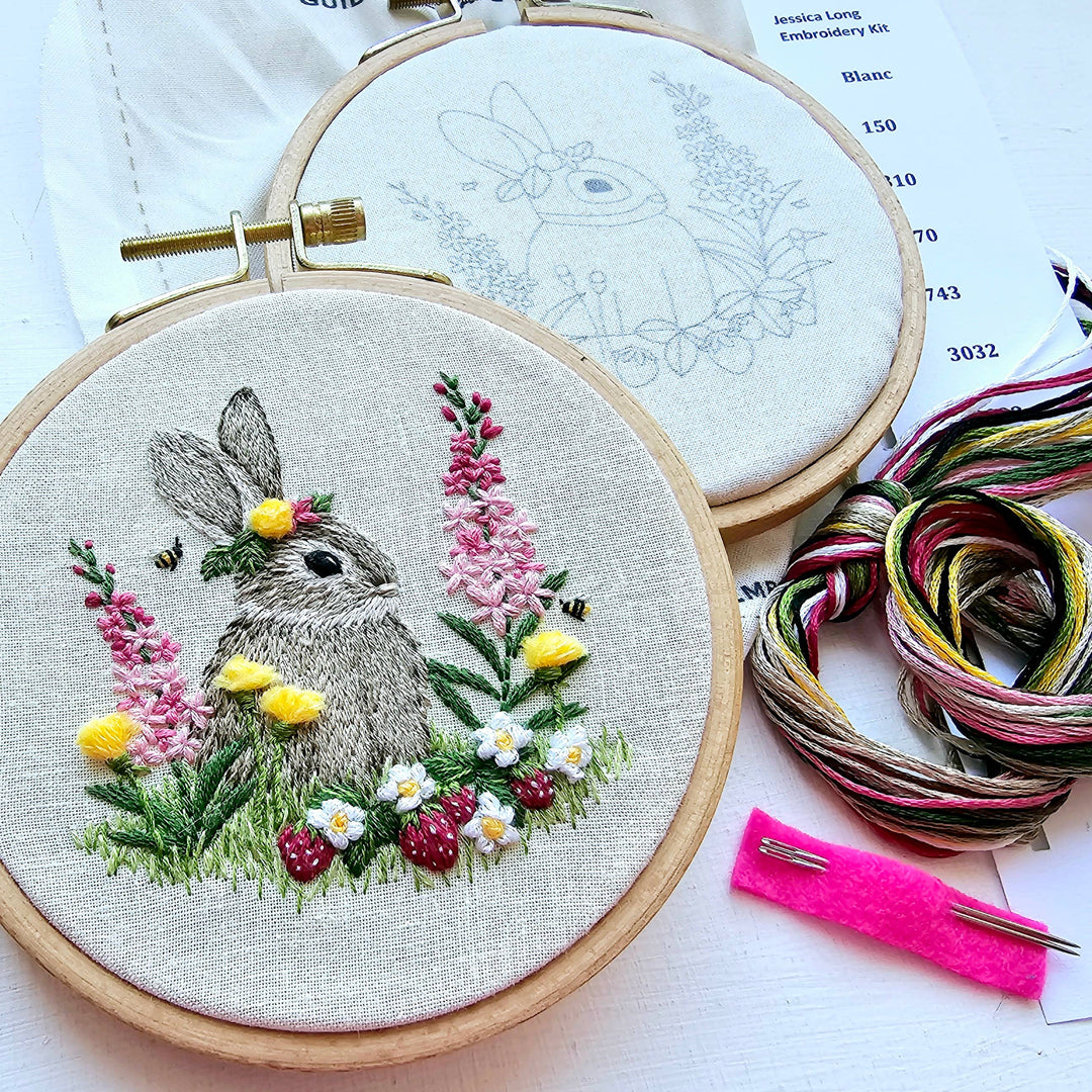 Embroidery hoop with a completed rabbit and floral design, surrounded by embroidery threads and tools.