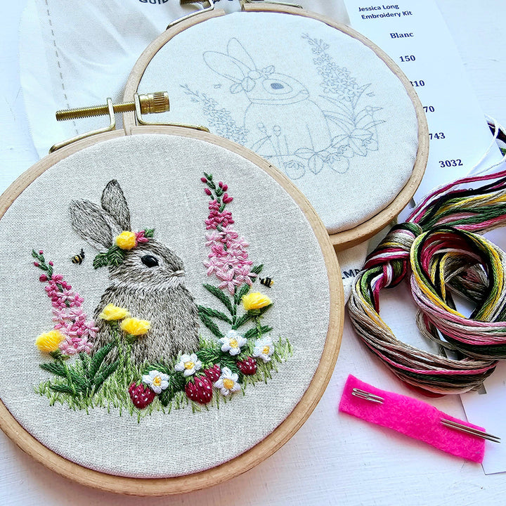Embroidery hoop with a completed rabbit and floral design, surrounded by embroidery threads and tools.