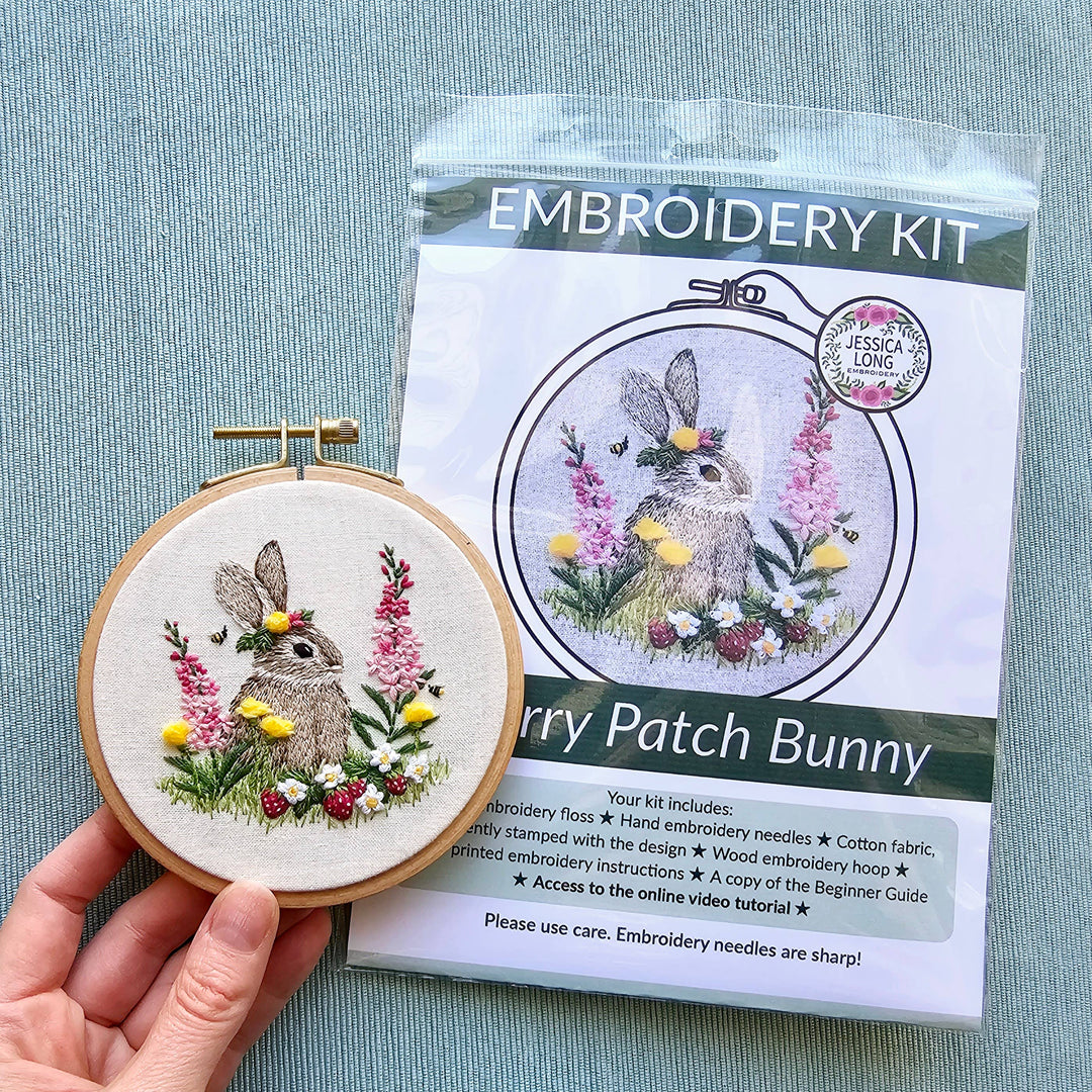 Embroidery hoop with completed bunny design and embroidery kit packaging on a blue background