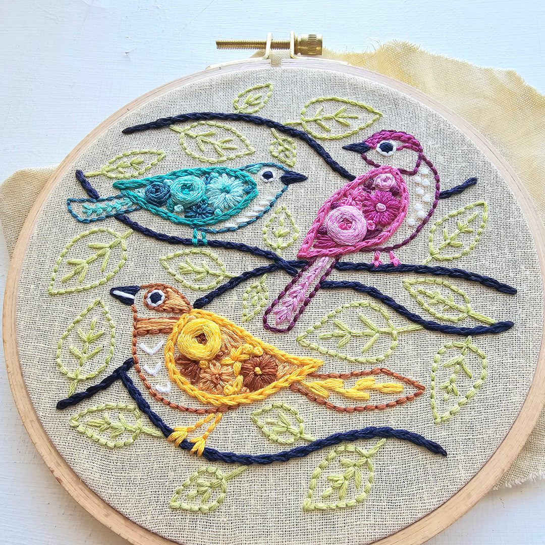 Embroidery hoop with colorful birds and leaves on a light background